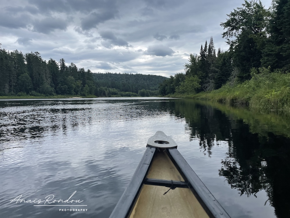 Vue depuis un canot sur une rivière et des collines sous les nuages