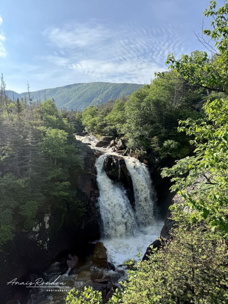 Chute d'eau au coeur des montagnes sous un ciel bleu sur le sentier du Gros-Morne