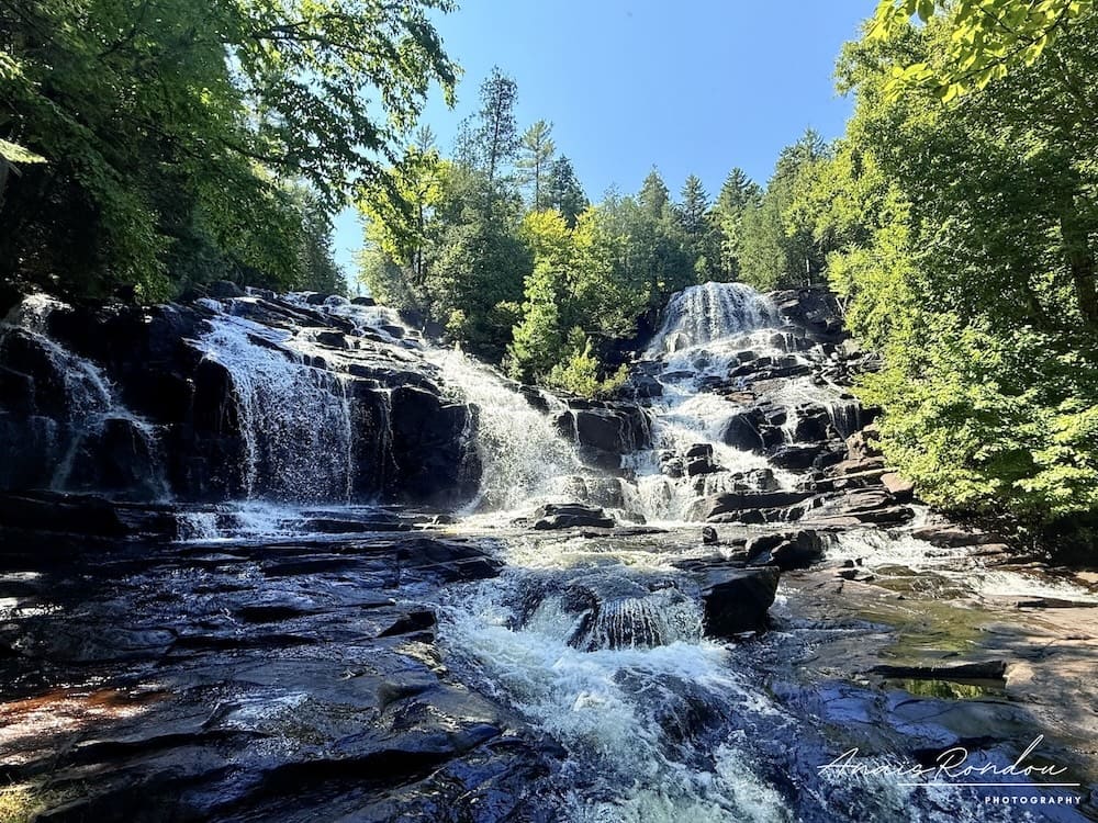 Chutes Waber qui s'écoule sur des rochers entre des arbres sous un ciel bleu