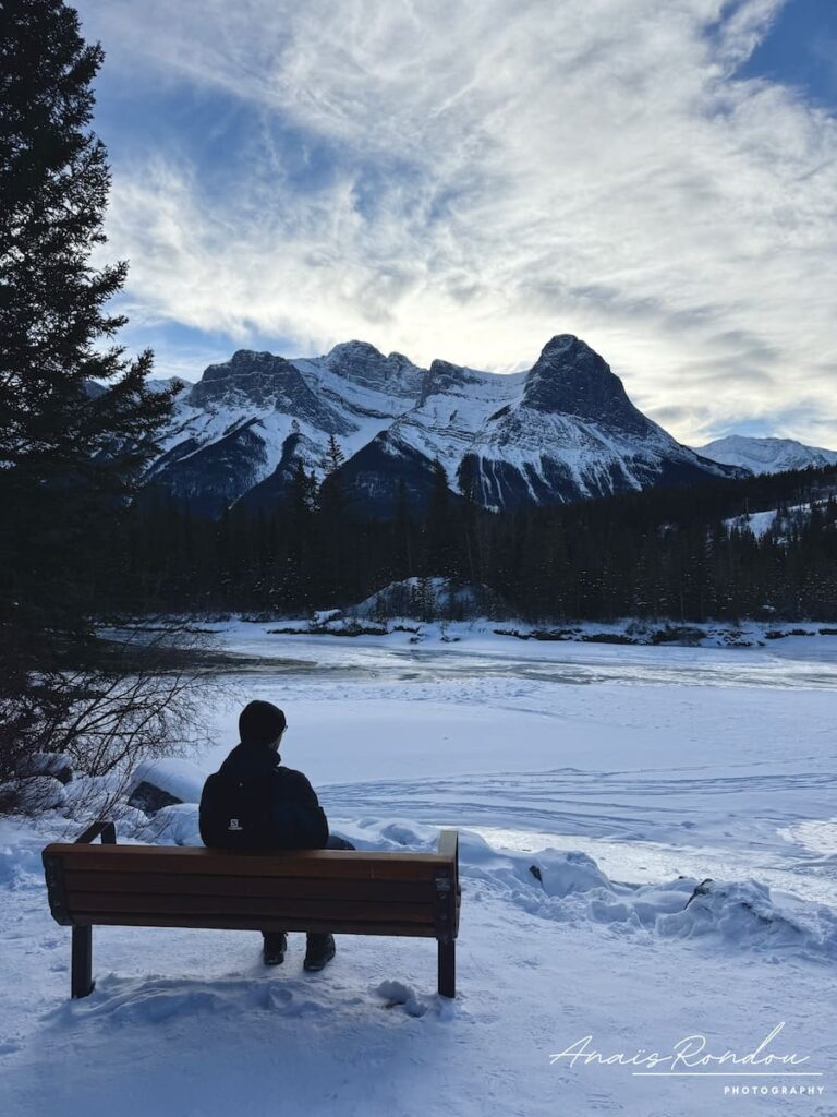 Personne assise sur un banc regardant les montagnes depuis la Bow River loop à Canmore