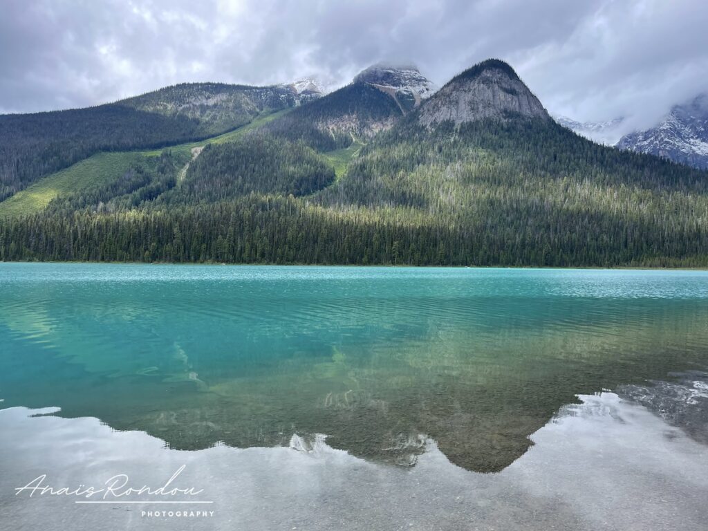 Lac Emeraude et sa couleur bleue intense avec des montagnes en fond sous les nuages